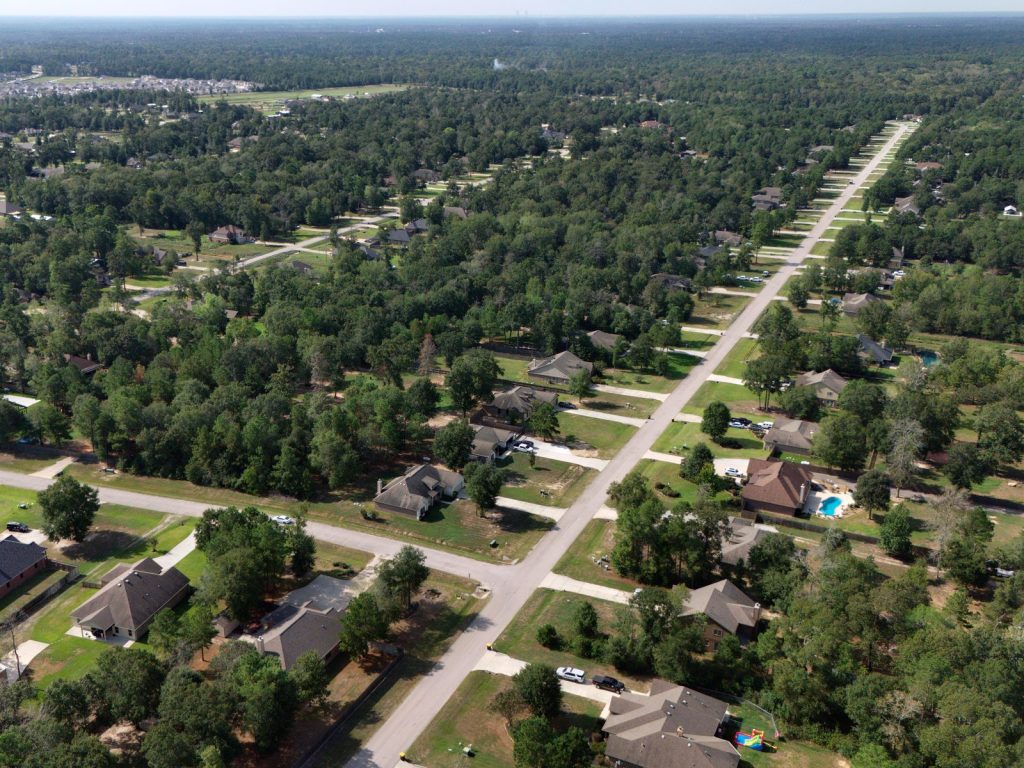 Aerial view of Deer Trail II homes along a straight street, with tall trees all around